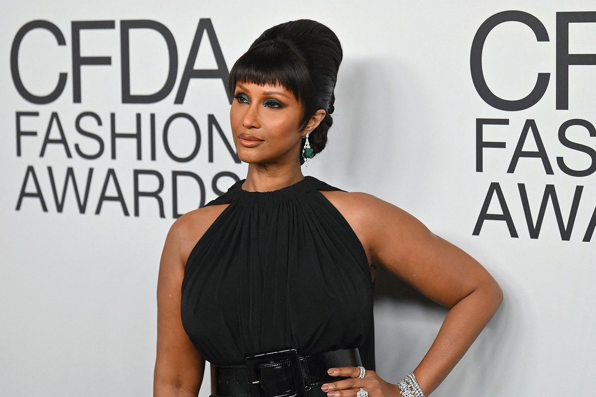An image of model Iman wearing a black dress posing on a red carpet