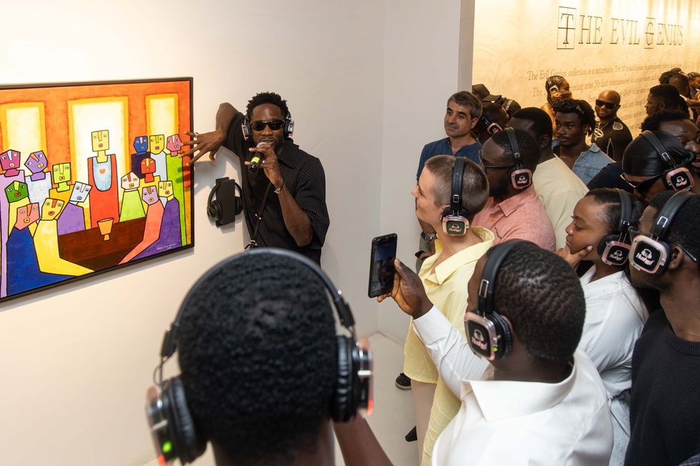 An image of Mr Eazi standing in front of Samuel\u2019s painting, speaking to people.