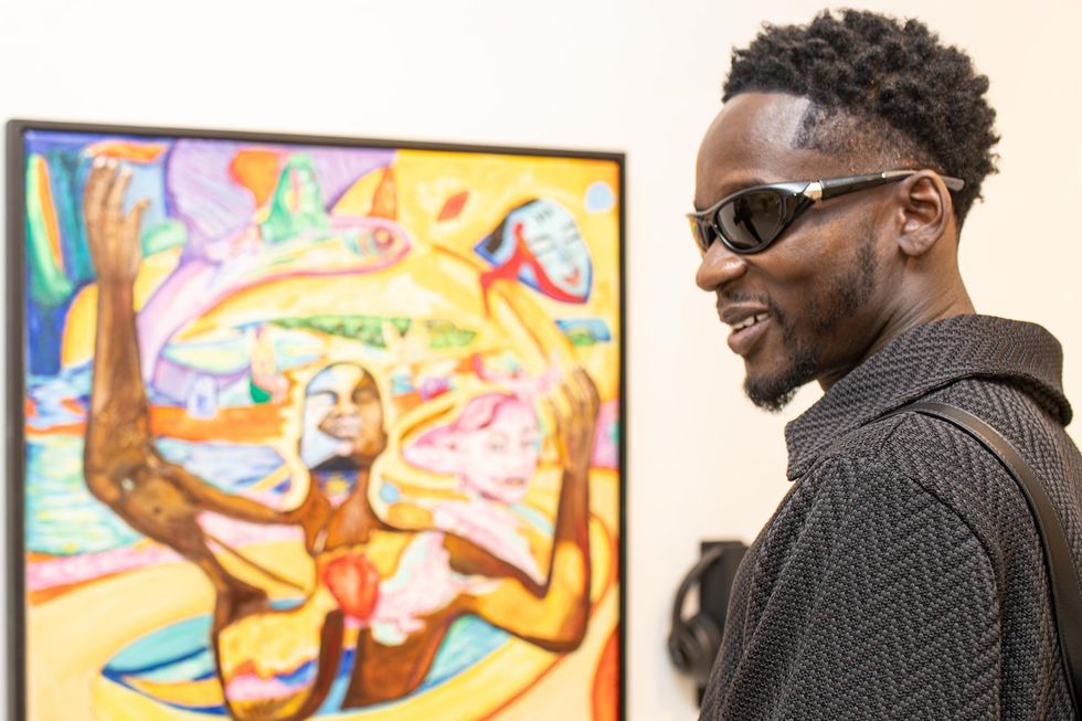 An image of Mr Eazi standing in front of the artwork in a gallery.