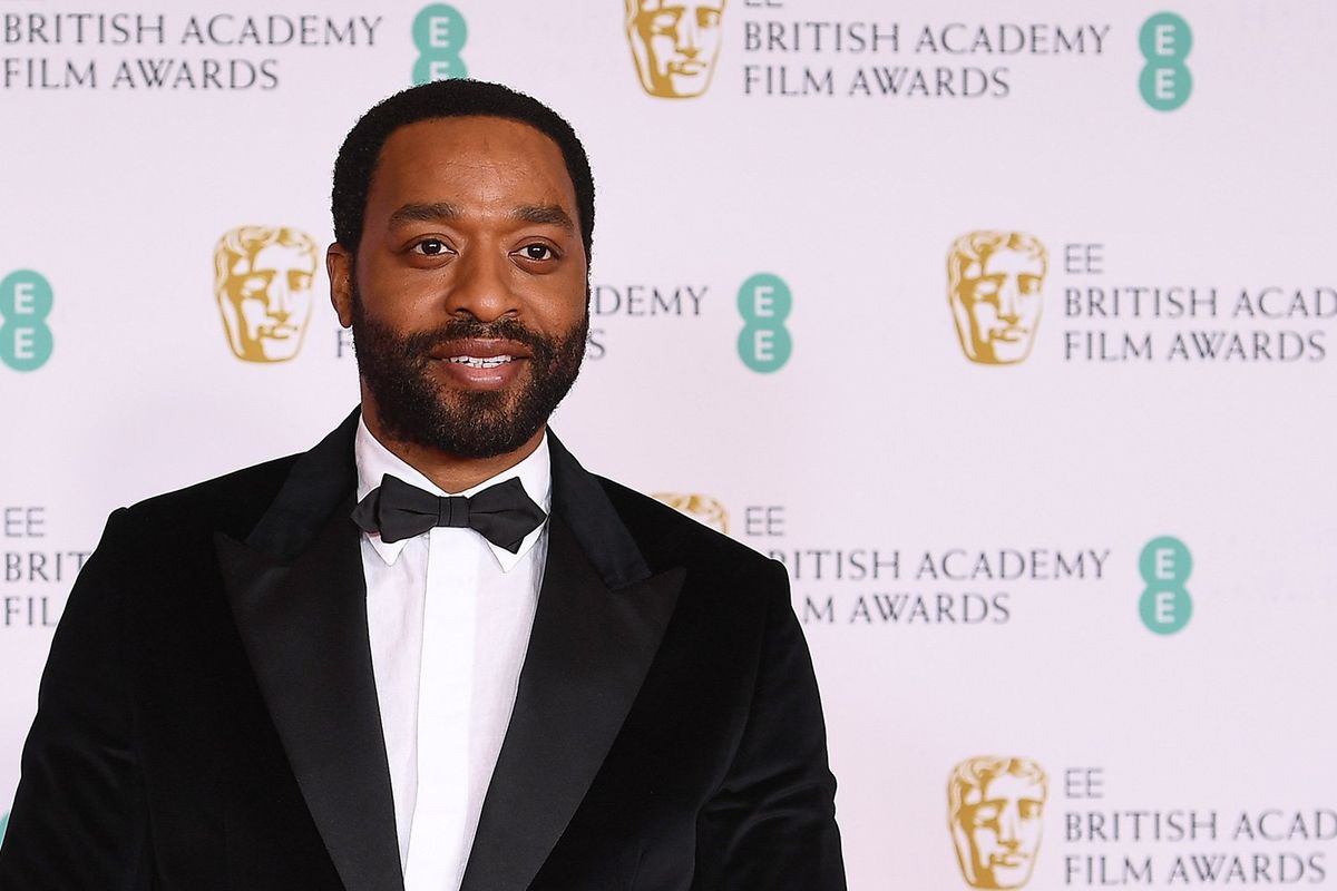 An image of the actor Chiwetel Ejiofor in a tux smiling at the camera on the red carpet of the British Academy Film Awards show. 