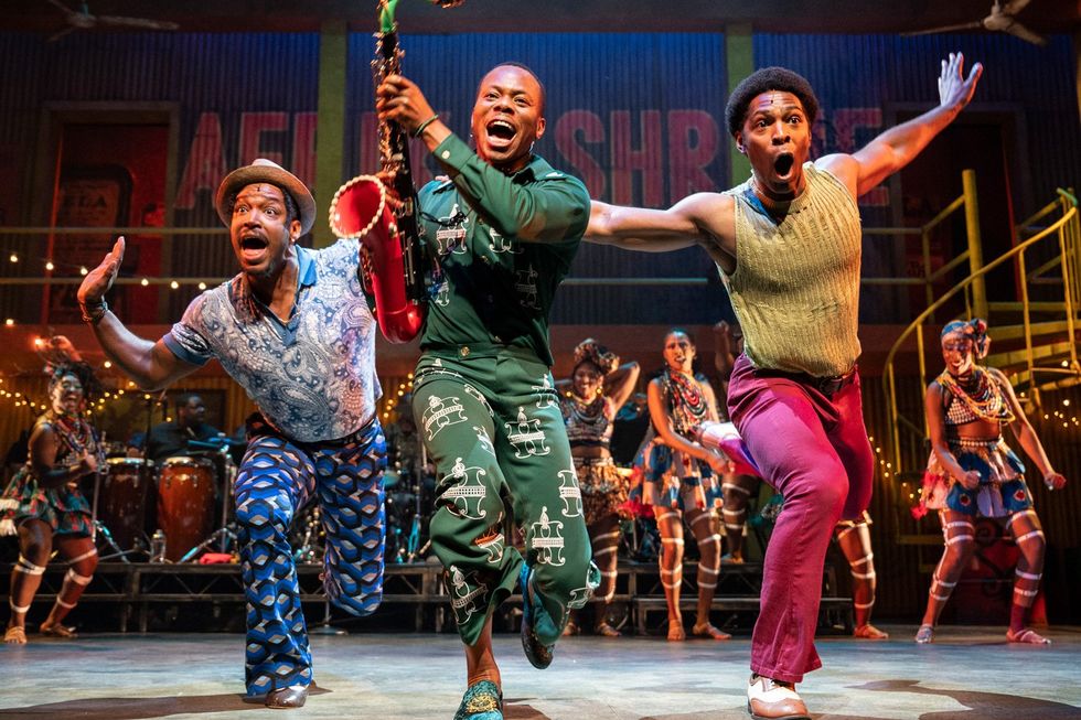 An image of the actor Duain Richmond lunging forward on stage as Fela, with a saxophone in his hand and two other actors by his side.