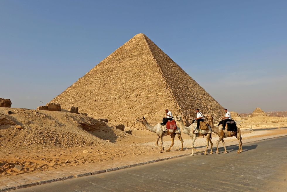 An image of three men riding camels past pyramids in Egypt