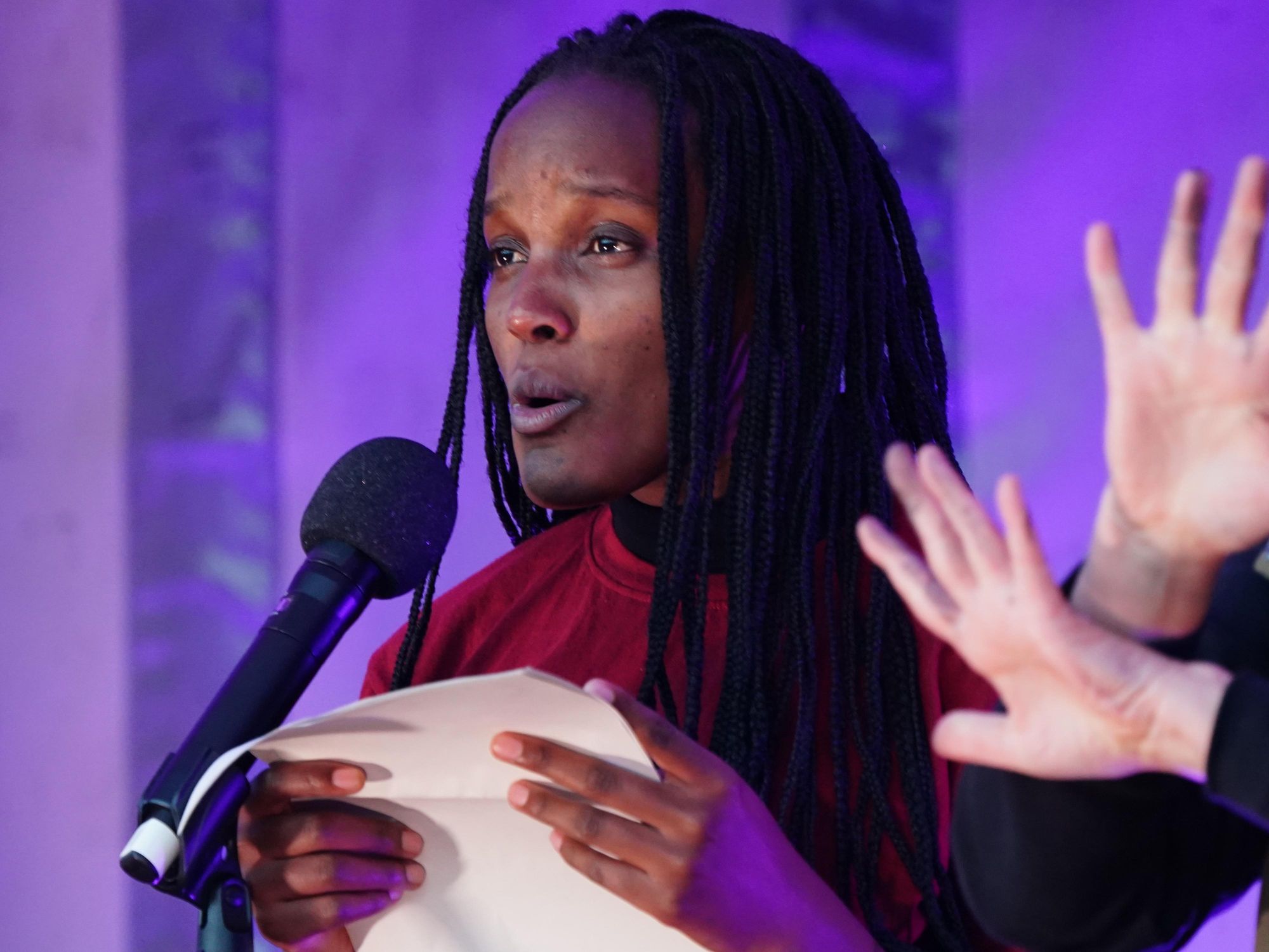 An image of ​Ugandan climate justice activist Vanessa Nakate talking at a microphone while holding a piece of paper.