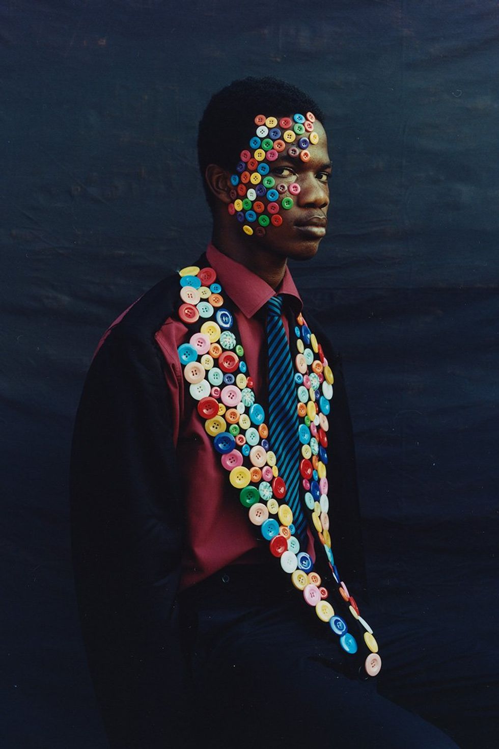 An image taken by the photographer of a man looking at the camera with buttons on the collar of his jacket and on one side of his face.