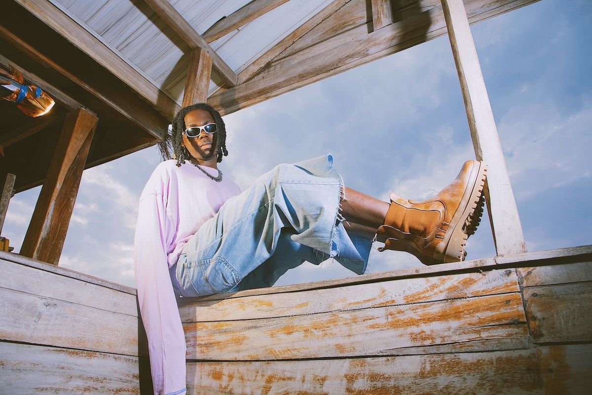 Bayanni poses in sunglasses and boots sitting on a wooden shed