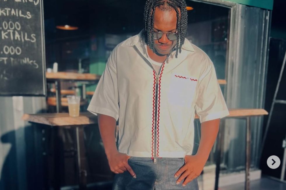 Bmjiah rocks braids, wears a white shirt, and blue jeans.