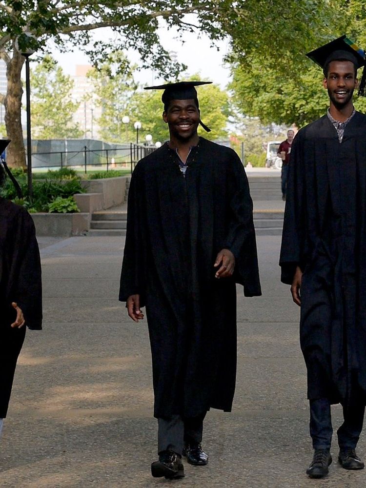 ‘Brief Tender Light’ stars Sante, Fidelis, Billy and Philip (left to right), dressed in graduation caps and gowns, walk towards the camera on the MIT campus.