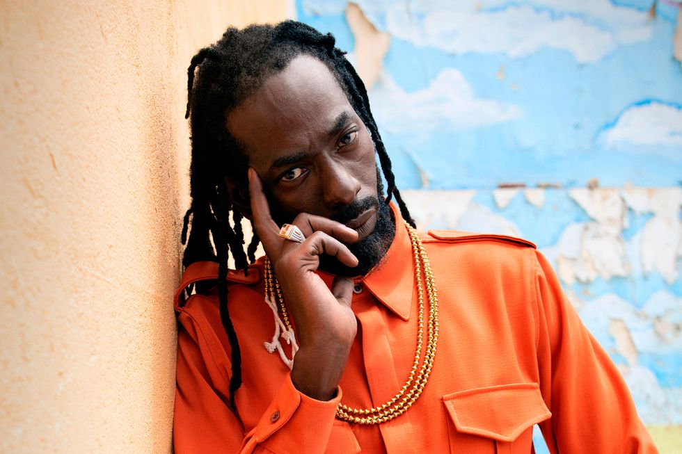 Buju Banton poses in front of a wall with a finger on his temple.