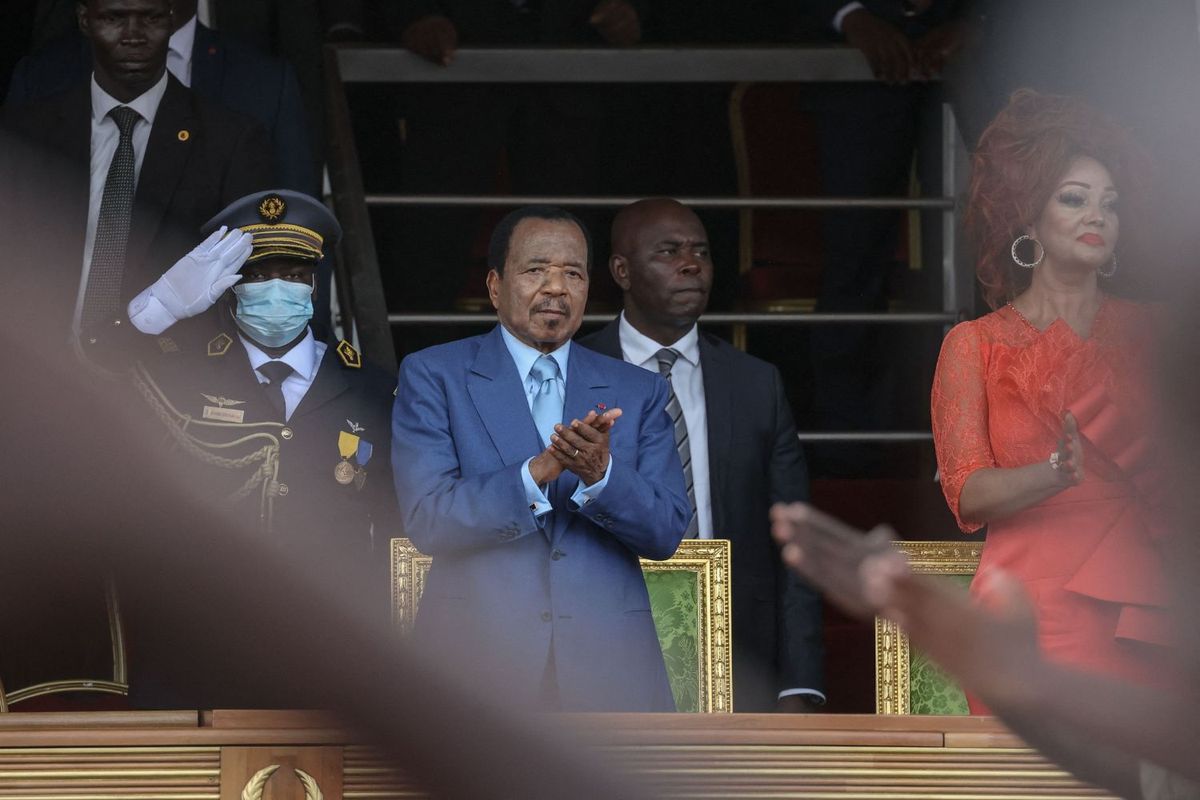 Cameroon President Paul Biya and his wife Chantal Biya applaud with a man dressed in a military uniform saluting in the background