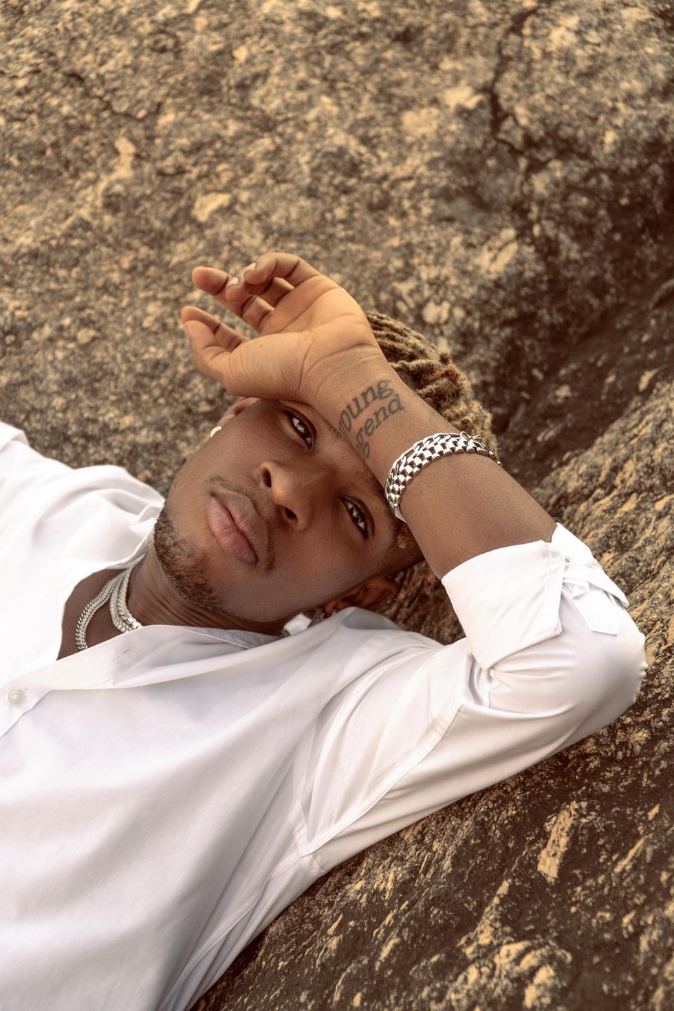 Close-up shot of Joeboy lying on a rock in a white shirt.