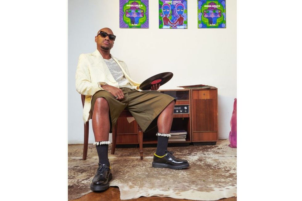 Da Capo sits on a chair facing the camera and holding a record in his hand