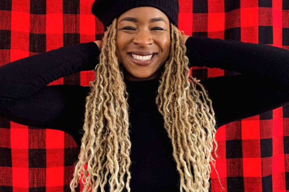 Deboh smiles for the camera while wearing a black dress, with her blonde braids peeking through her black beret.