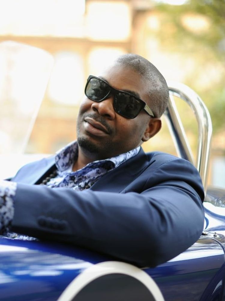 Don Jazzy leans out the side of a blue convertable car wearing a slick blue suit.