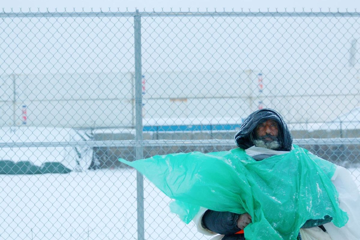 Eshete stands in front of a chain link fence, he is wrapped in large plastic sheets while it snows.