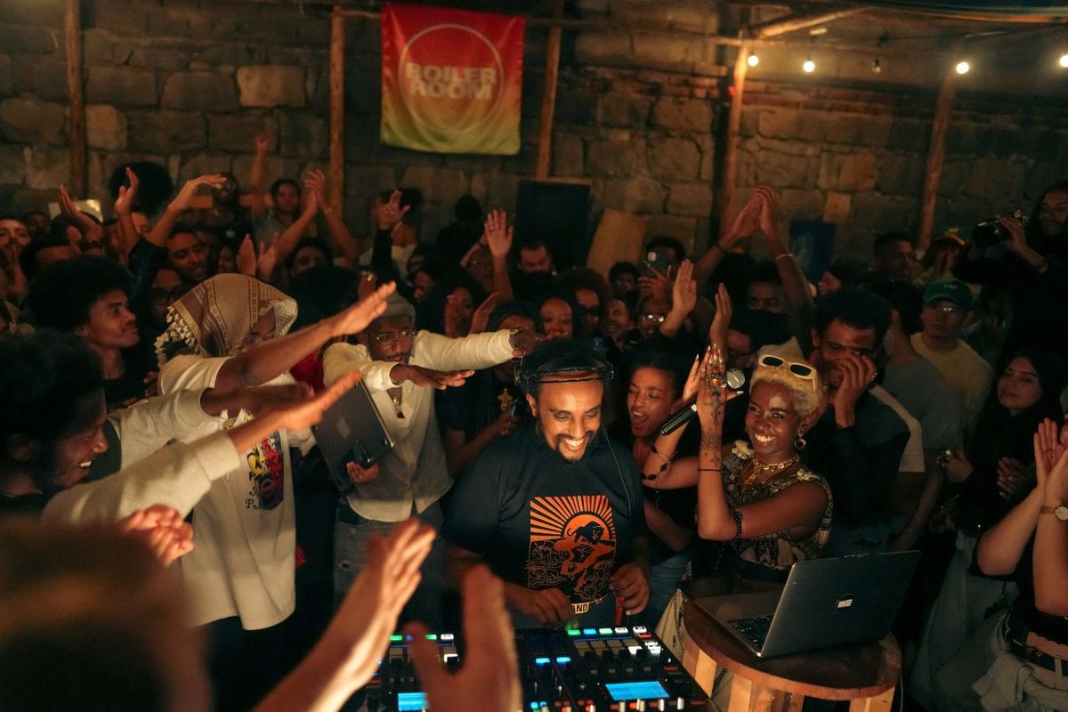 Ethiopian Records stands at the center of a lively crowd during a Boiler Room performance in Addis Ababa, smiling as people cheer and raise their hands around him.
