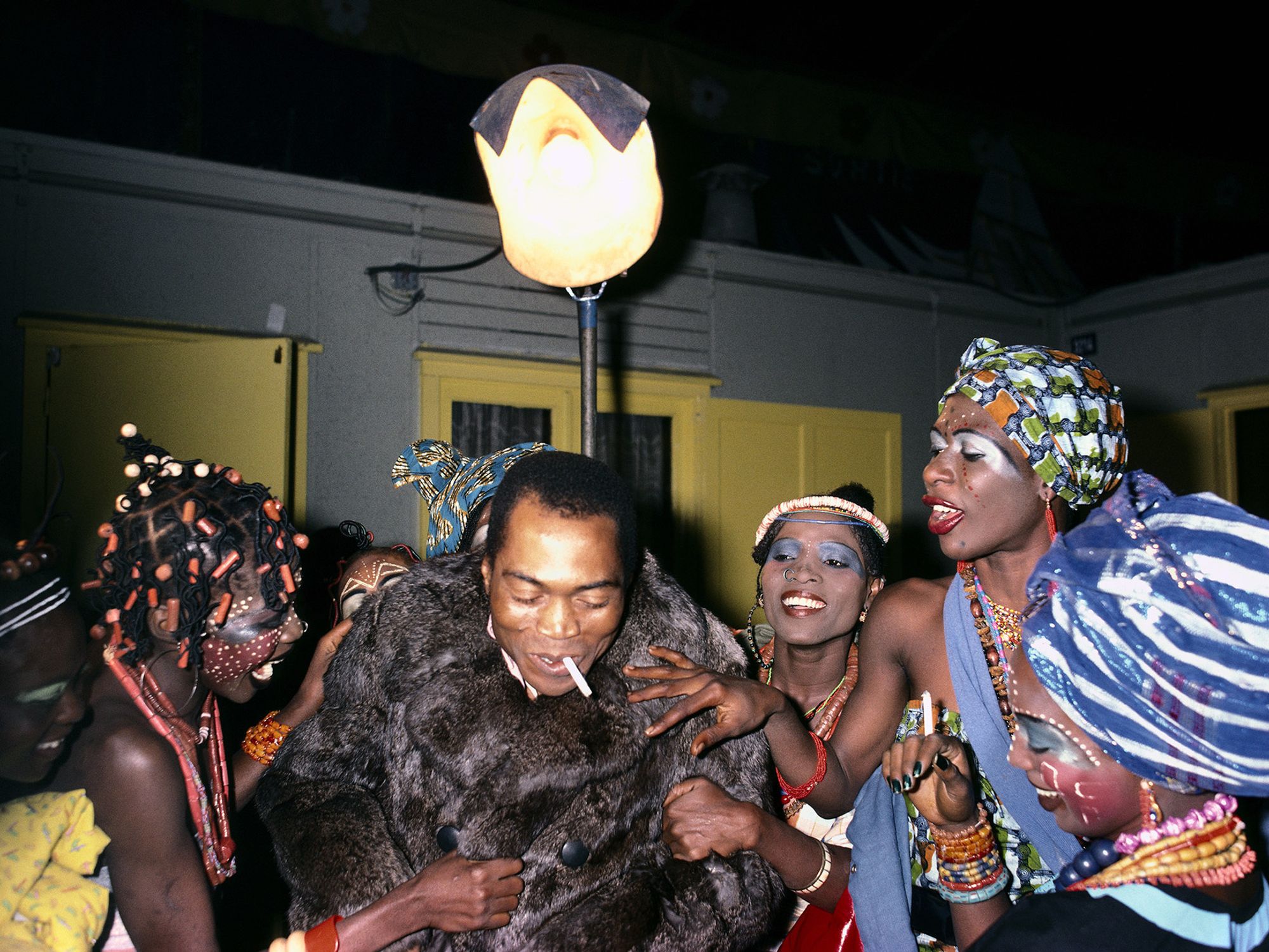 Fela Kuti in fur jacket surrounded by the Kalakuta Queens in African headwraps, facepainting and braids.