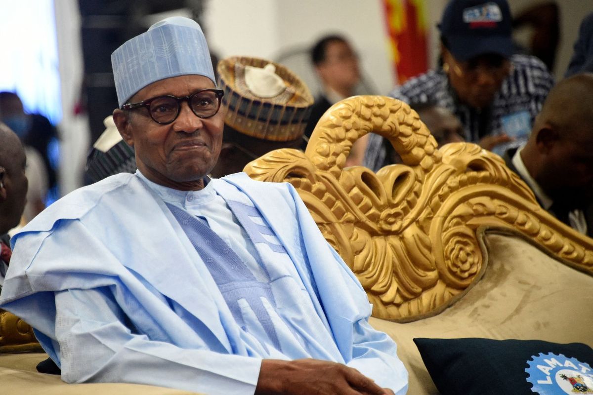 Former Nigerian President Muhammadu Buhari smiling as he sits on a chair with a gold edge and wears a blue outfit.