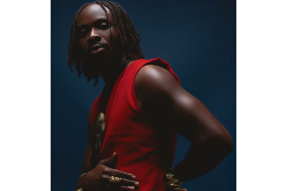 Fuse ODG is seen wearing a sleeveless red jacket and pants behind a dim, deep blue backdrop.