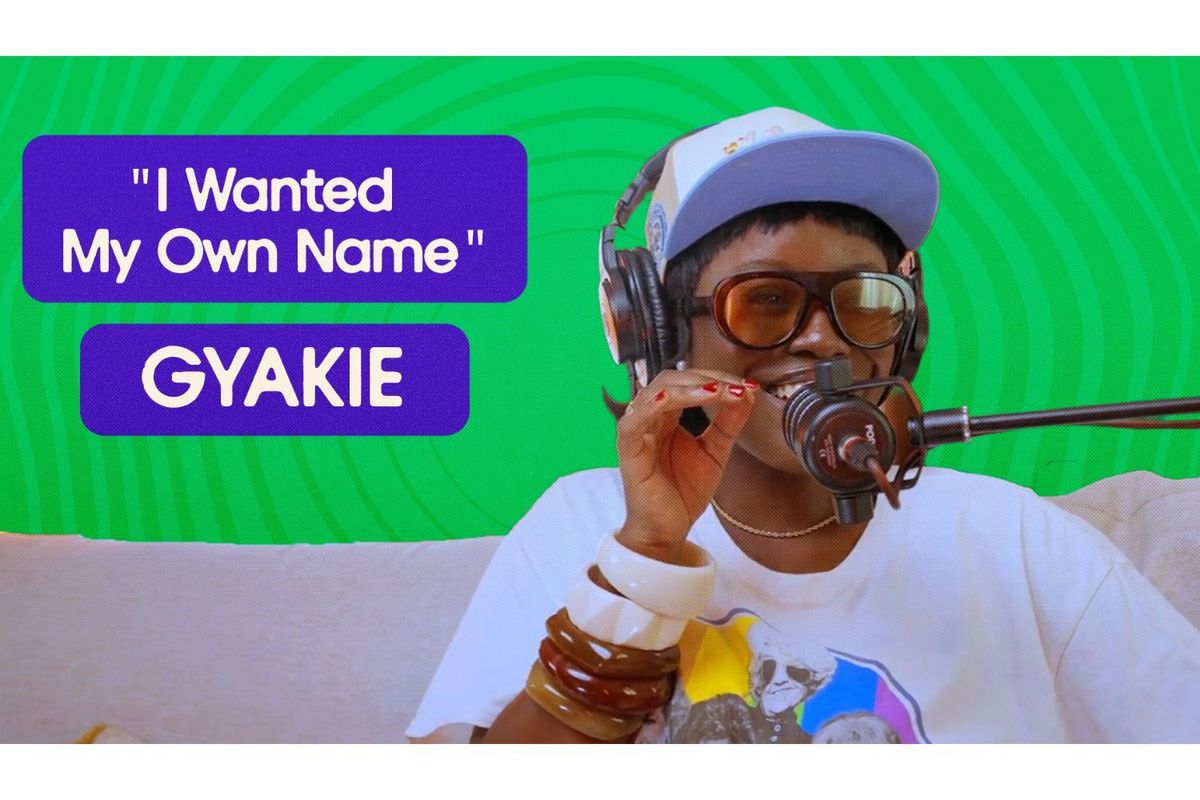 Ghanaian singer Gyakie smiles while recording a podcast interview. She wears oversized sunglasses, a cap, headphones, and colorful bangles. A quote on screen reads “I Wanted My Own Name” with her name “GYAKIE” in bold, set against a bright green background.
