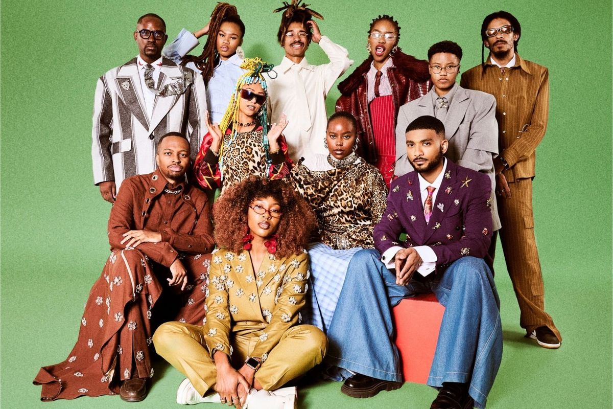 Group portrait of stylishly dressed young Black creatives posing against a green backdrop.