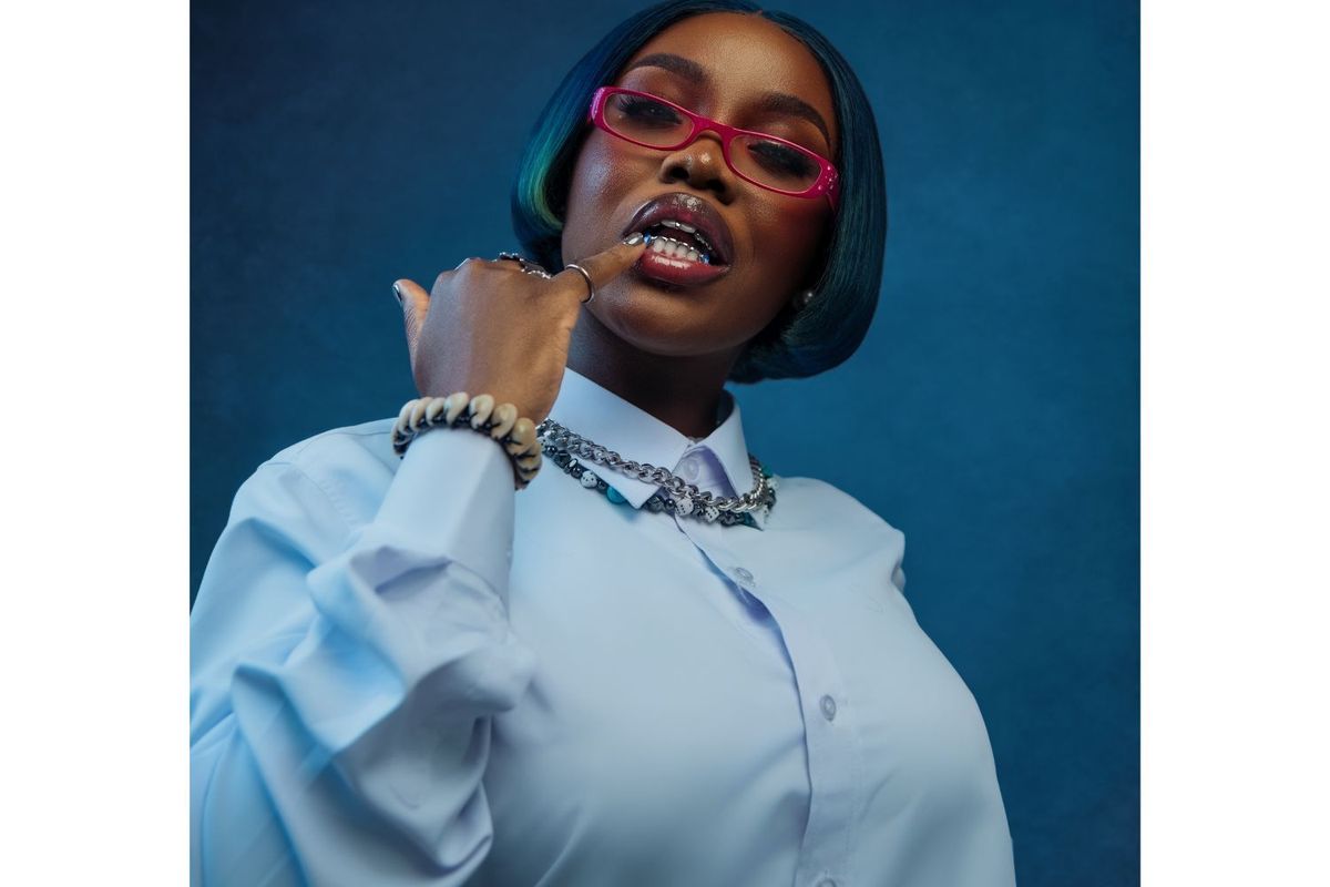 Gyakie poses in a promotional shot wearing grills in her mouth and sporting blue hair.