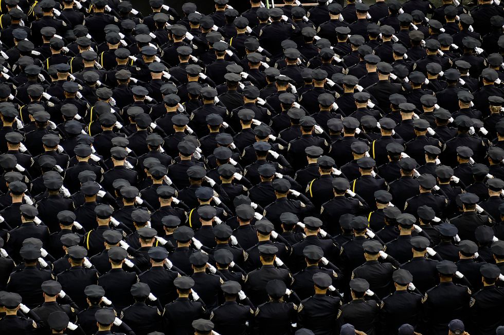 Hundreds of police stand in formation wearing ceremonial uniforms.