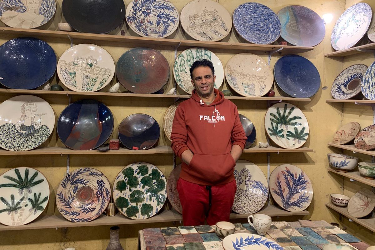 Ibrahim Samir stands in front of shelves of decorative plates in his workshop in Tunis. 