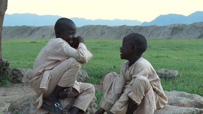  An image from the documentary of two brothers sitting in a field laughing with each other. 