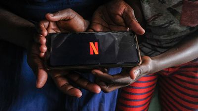 An image of two hands holding a phone with the Netflix logo on it. 