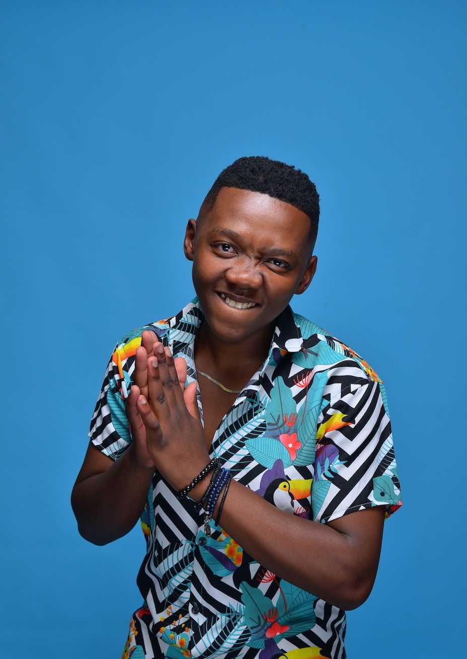 A portrait of Aymos rubbing his hands wearing a blue Hawaiian shirt and standing in front of a matching backdrop. 