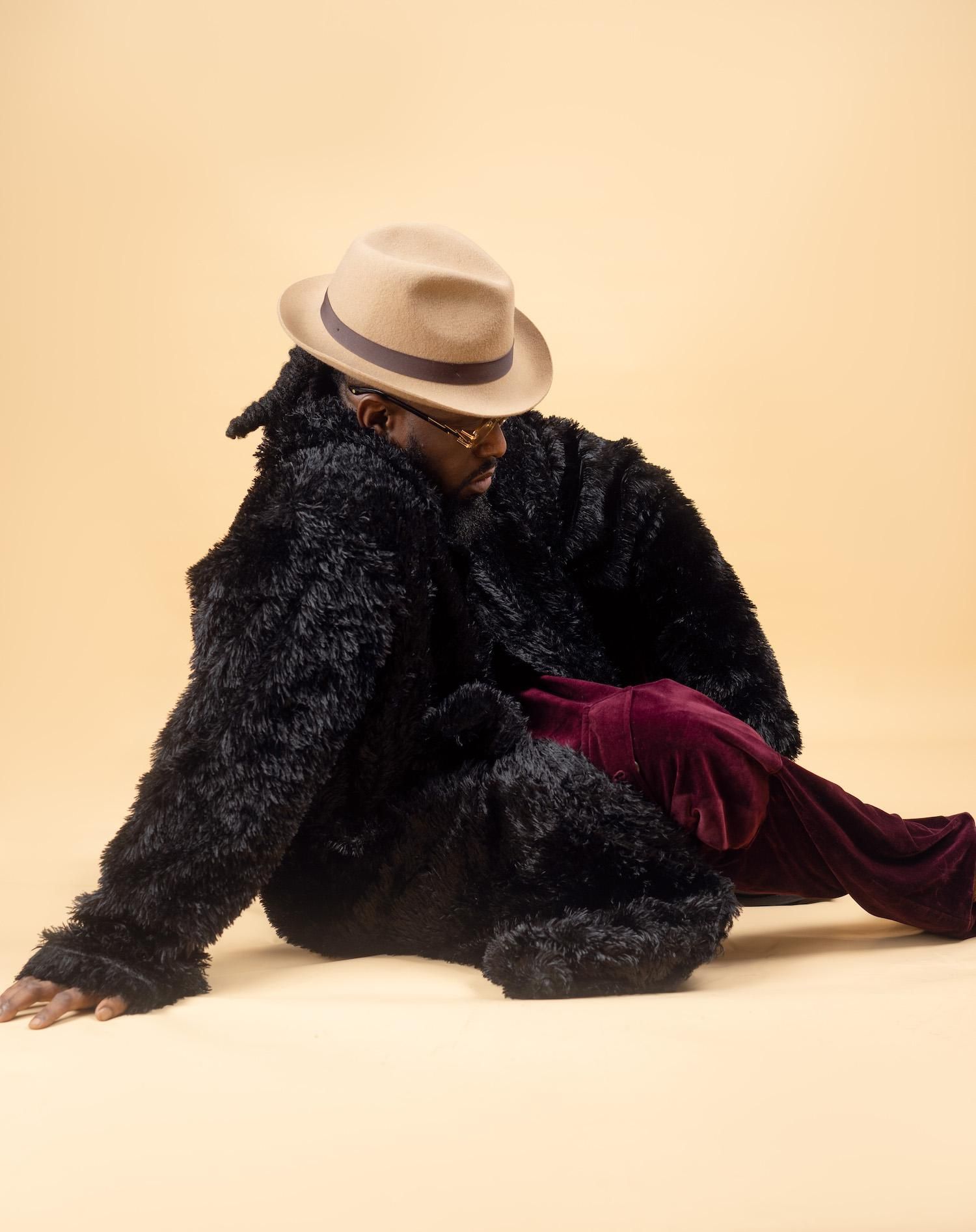 Nigerian artist Timaya sits in a yellow background with a black fur coat.