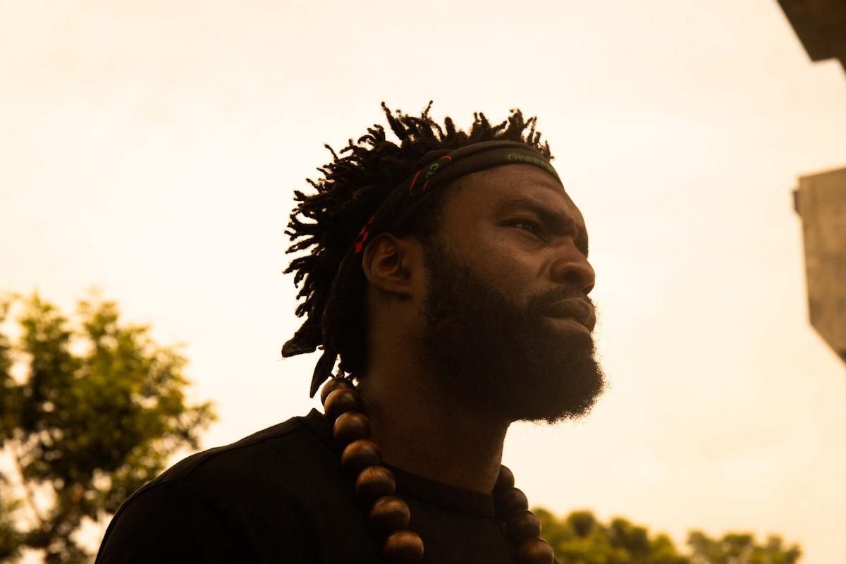 Profile picture of music video director Meji Alabi. He wears a bandana on his forehead and large bead necklace over black t-shirt.