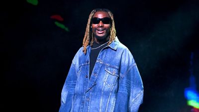 Asake smiles in a denim jacket and black shades. 