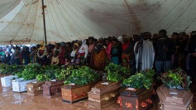 Mourners stand behind coffins of their relatives during a mass funeral for mudslide victims at Chilobwe townships Naotcha Primary school camp in Blantyre, Malawi, on March 15, 2023