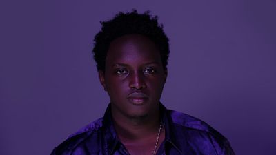 Ugandan artist Joshua Baraka poses in a purple shirt.