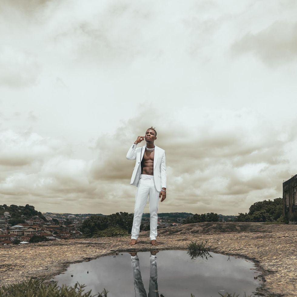 Joeboy stands on a field in front of a puddle.