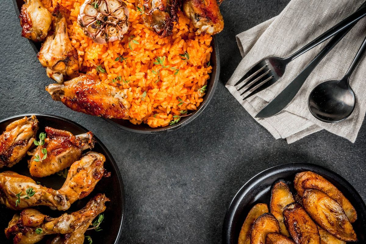 Jollof rice with grilled chicken wings and fried bananas plantains on gray stone table.
