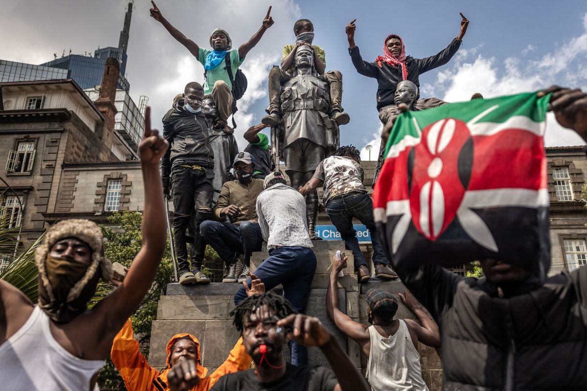 Kenya protestors holding up flags and the middle finger, climb a statue in the city center during demonstrations.