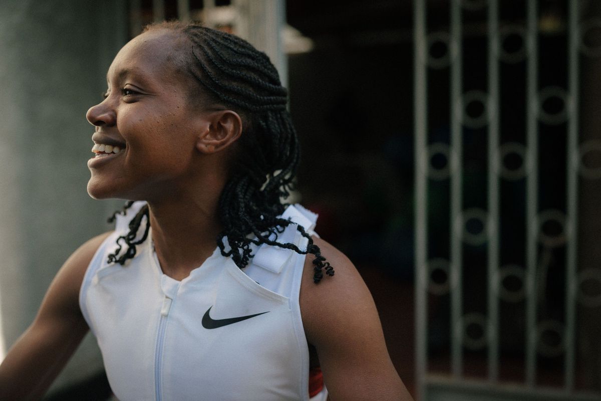 Kenyan Olympian Faith Kipyegon, wearing a white vest, looks off to the side smiling.