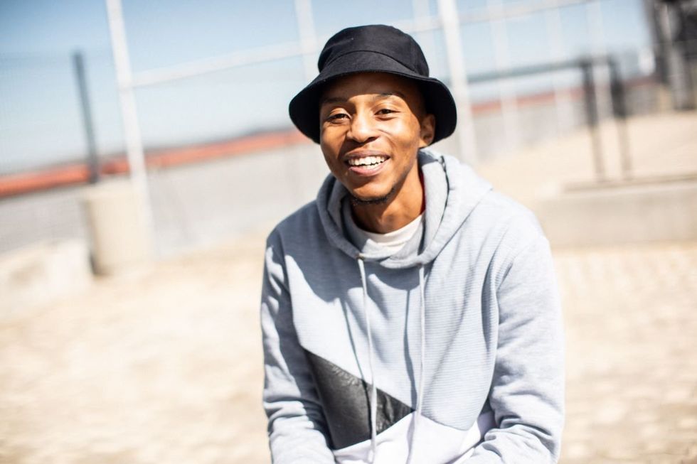 Kgotso Motingwe smiles in a grey hoodie and a black bucket hat.