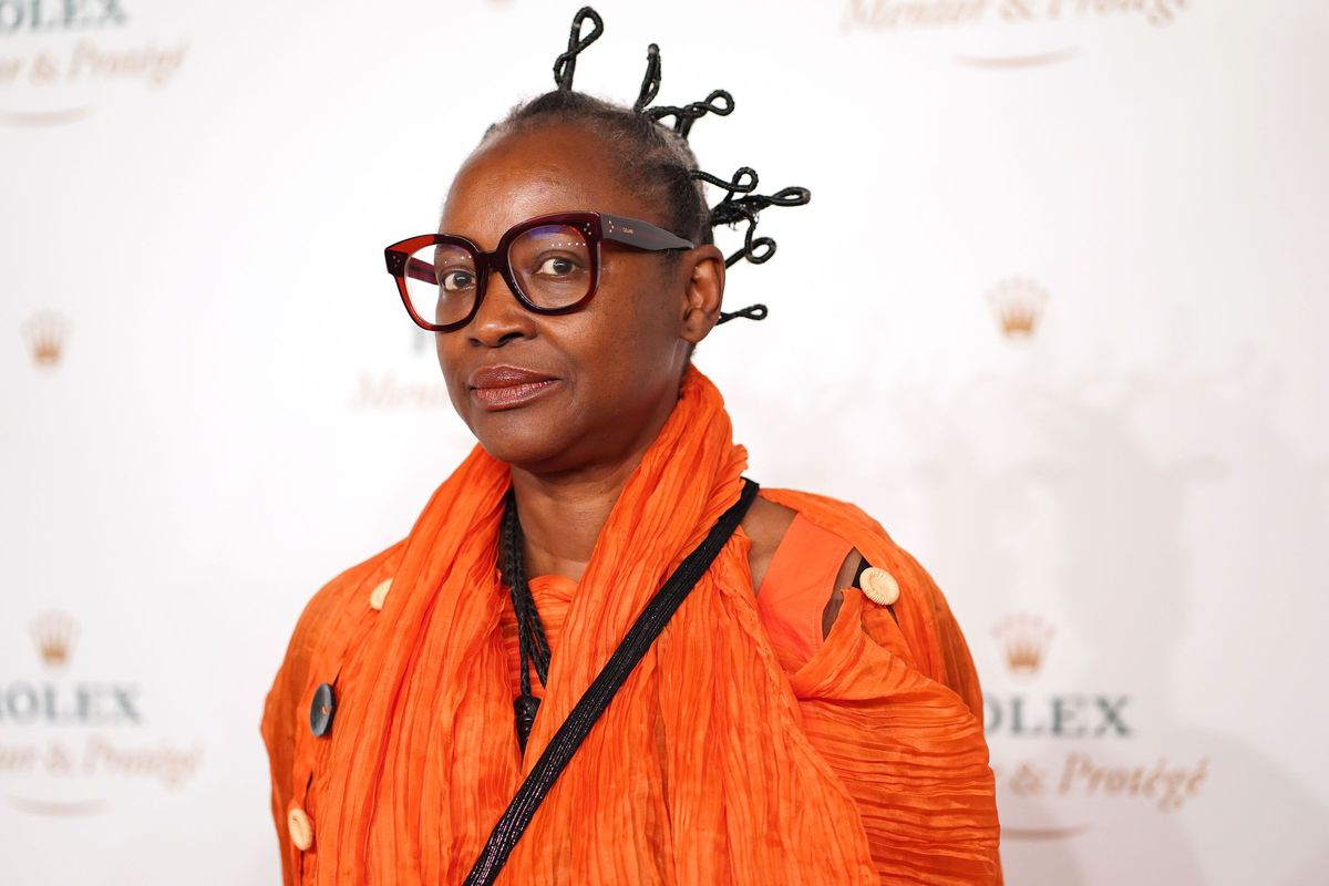 Koyo Kouoh in an orange dress and glasses staring at the camera