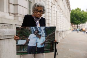 Laila Soueif stands on a city sidewalk holding a large photograph of herself with a man in front of a waterfall, both smiling and embracing.