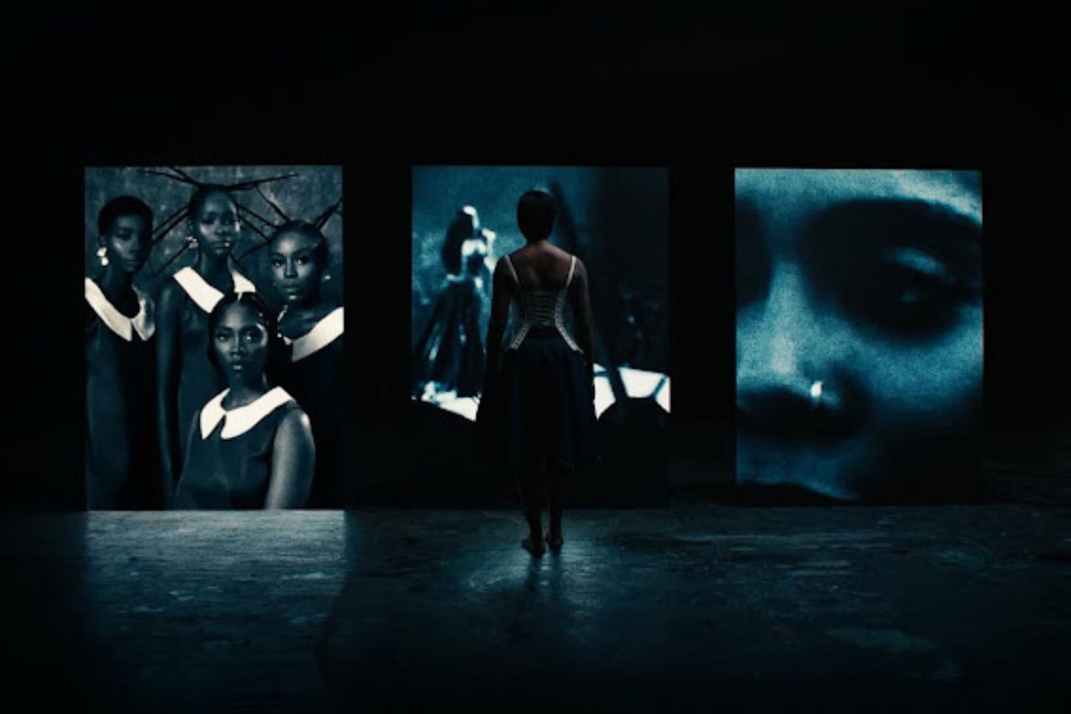 A woman stands in the shadow in front of three large screens.