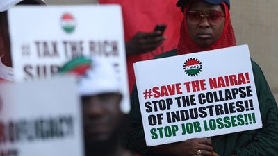 A woman holds a placard that reads “Save The Naira, Stop The Collapse Of Industries!! Stop Job Losses!!!” during a protest against the soaring cost of living in Abuja on February 27, 2024