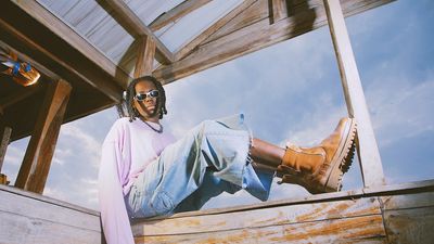 Bayanni poses in sunglasses and boots sitting on a wooden shed