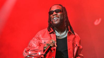 burna boy wearing red onstage performing and smiling