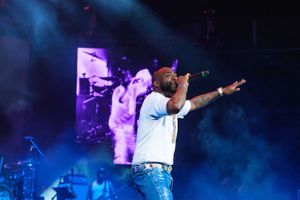 Davido performs on stage, wearing blue jeans and a white shirt, mic in hand, band in the background