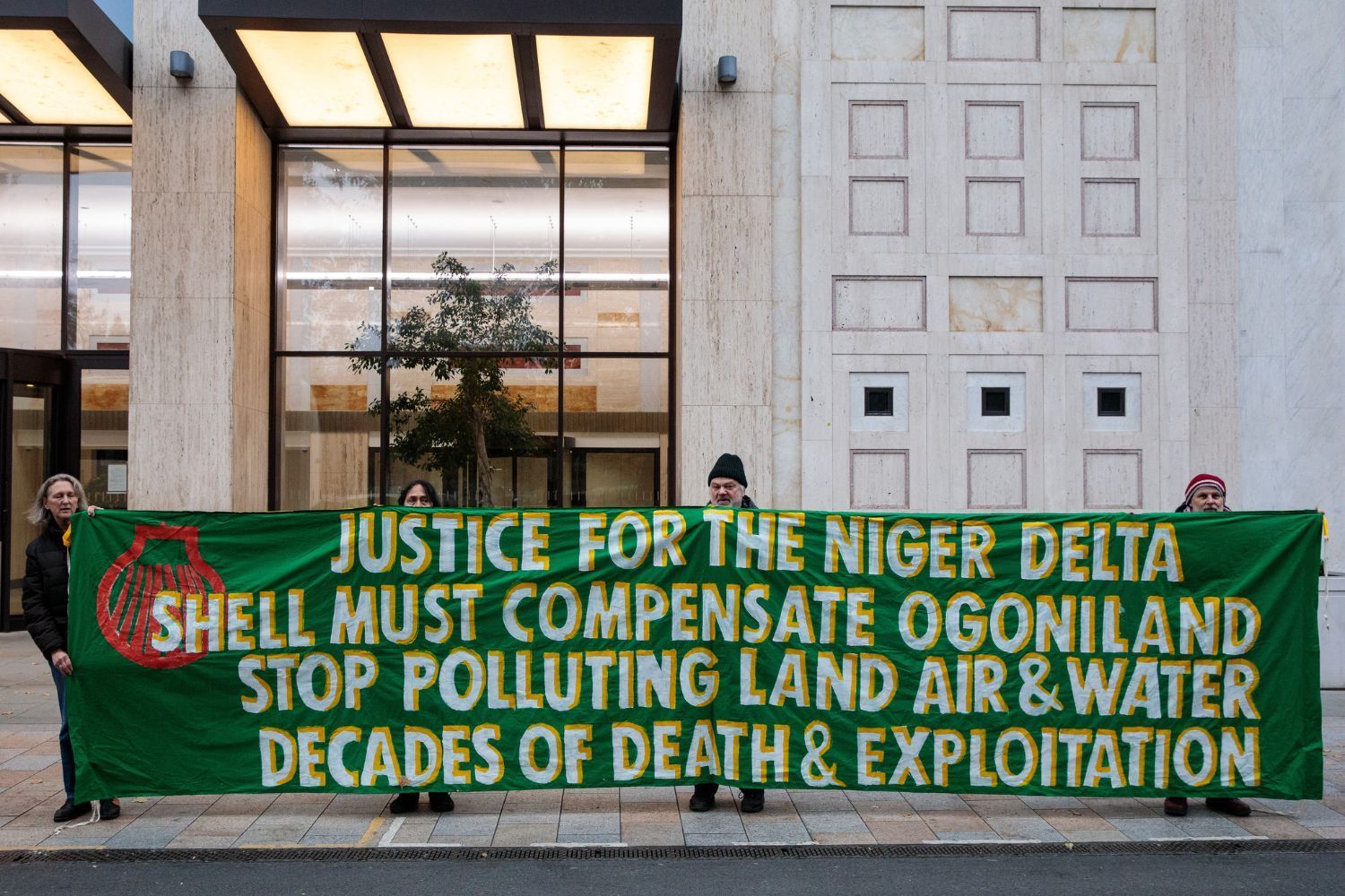 Protesters hold a large banner outside a building demanding justice for the Niger Delta and compensation from Shell for decades of pollution and exploitation in Ogoniland.