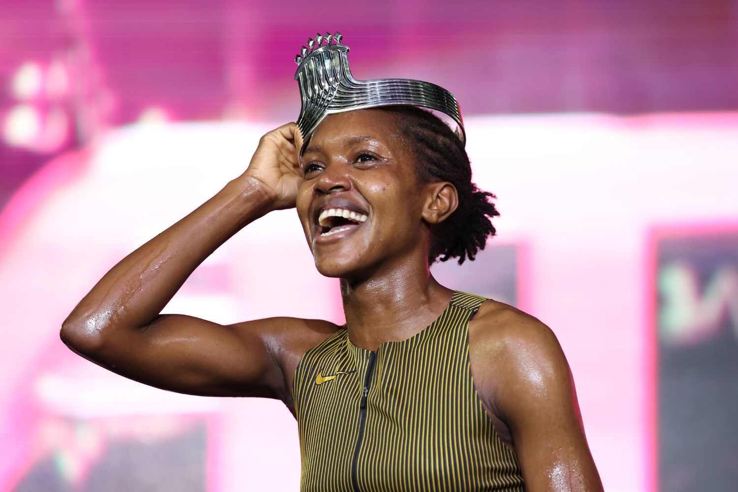 A joyful athlete, glistening with sweat, smiles broadly while wearing a unique silver crown atop her head, celebrating a victory.
