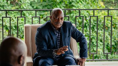 Joseph Kabila gestures with his hand as he talks, he sits on a beige-colored chair with green trees behind him